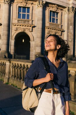 sunshine on face of pleased young woman with backpack near bode museum in berlin  clipart