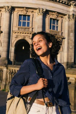 sunshine on face of amazed young woman with backpack near bode museum on museum island