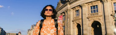 stylish young woman in sunglasses standing near building on museum island, banner