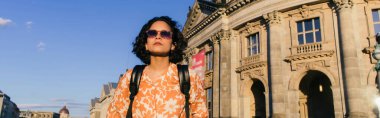 stylish young woman in sunglasses standing near building on museum island, banner clipart