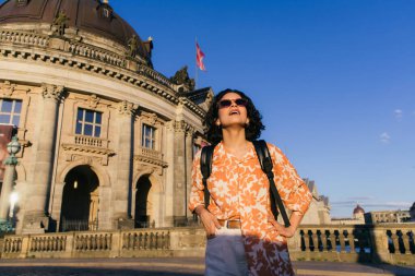 amazed young woman in sunglasses standing near building on museum island clipart