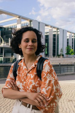 smiling young woman with backpack standing near modern contemporary building in berlin
