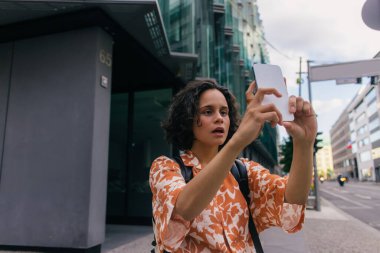 curly tourist with open mouth using smartphone in berlin 