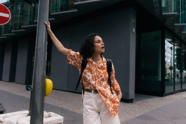 curly young tourist with backpack standing on urban street in berlin 