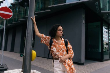 curly young woman with backpack standing on urban street in berlin 
