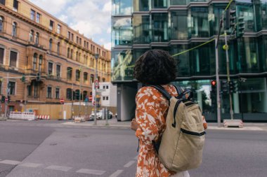 back view of curly young woman with backpack standing on urban street in berlin 