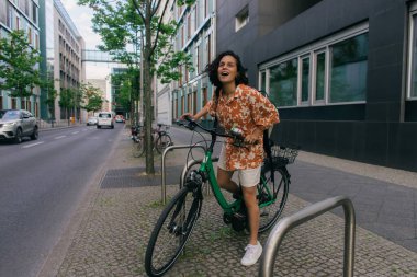 full length of amazed young woman in summer outfit riding bicycle in berlin 