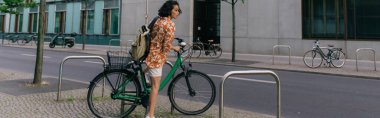 amazed young woman in summer outfit riding bicycle on street in berlin, banner