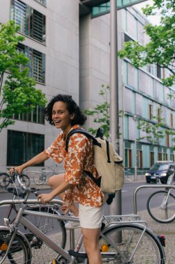 excited young woman in summer outfit riding bicycle on street in berlin 