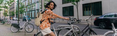 curious young woman in summer outfit standing near bicycle in berlin, banner
