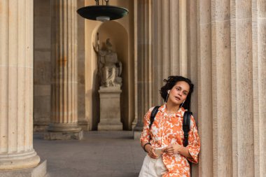 traveler in wired earphones listening music and holding smartphone near statue in berlin