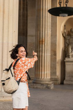 happy traveler in earphones listening music and pointing at statue in berlin