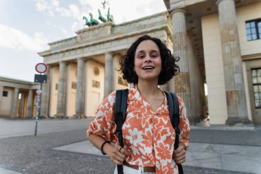 cheerful tourist with backpack standing near brandenburg gate in berlin 