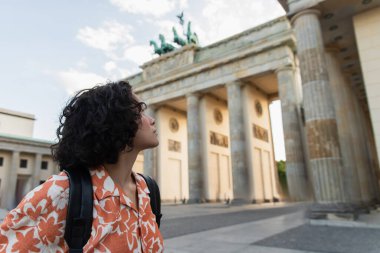 young traveler with backpack looking at brandenburg gate in berlin 