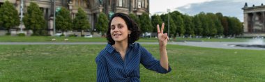 happy young woman with laptop showing peace sign in berlin, banner