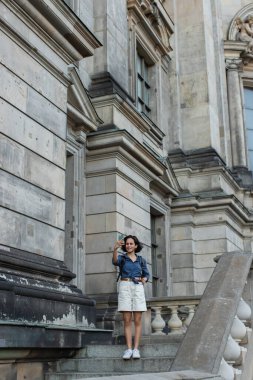 full length of happy tourist taking selfie on smartphone in front of building in berlin 