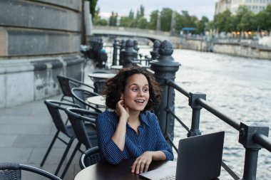 happy young freelancer using laptop while sitting on summer terrace near river in berlin 