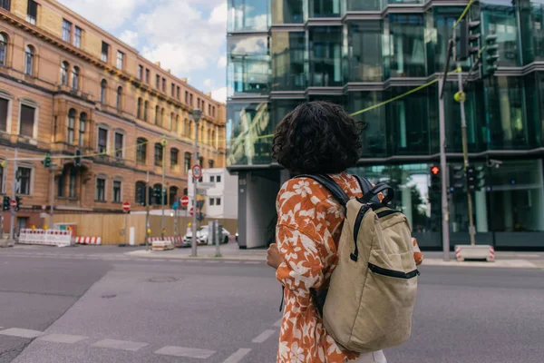 back view of curly young woman with backpack standing on urban street in berlin 