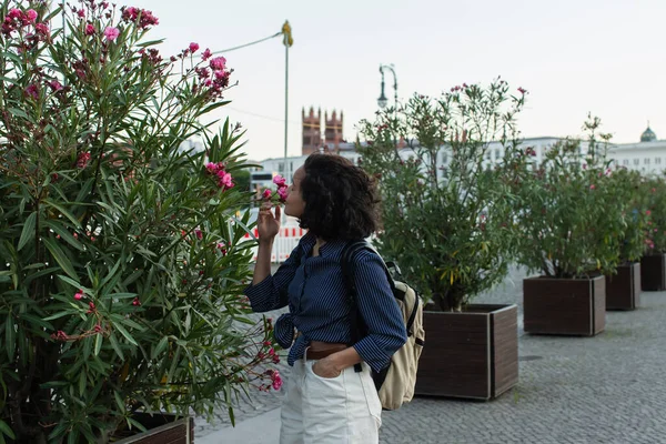 Curly Young Woman Backpack Smelling Flower Standing Hand Pocket Street — Foto de Stock
