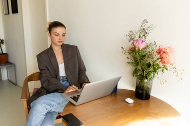 Akıllı telefonun ve çiçeklerin yanında dizüstü bilgisayar kullanan genç bir kadın. 