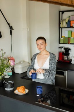 Genç bir kadın ayçöreği yanında fincanı ve mutfakta çiçekleri tutuyor. 