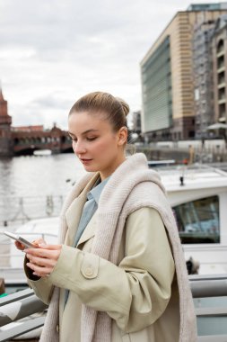 Berlin 'de şehir sokağında cep telefonu kullanan trençkotlu bir kadın. 