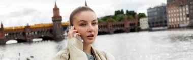 Berlin 'de trençkotlu genç bir kadın akıllı telefondan konuşuyor. 