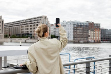 Berlin 'de, trençkotlu bir kadının cep telefonuyla fotoğraf çekişi. 