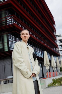 Trençkotlu genç bir kadın Berlin 'deki şehir sokağına bakıyor. 