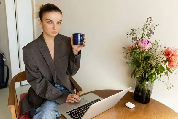 Mujer Con Chaqueta Sosteniendo Taza Mirando Cámara Cerca Computadora Portátil — Foto de Stock