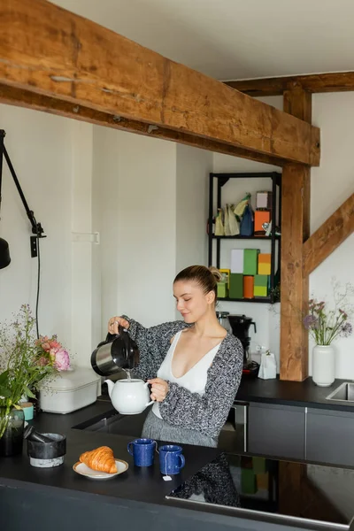 Mujer Sonriente Vertiendo Agua Tetera Cerca Sabroso Croissant Tazas Cocina — Foto de Stock