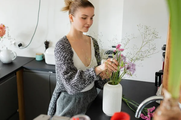 Evde Vazoya Çiçek Koyan Örülü Hırkalı Genç Bir Kadın — Stok fotoğraf