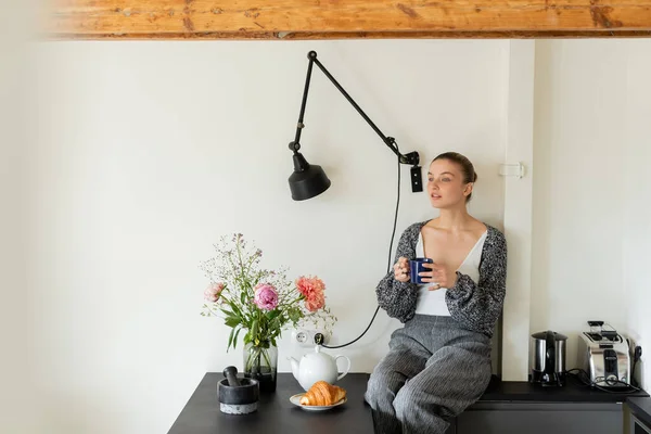 Kvinna Stickad Kofta Innehav Kopp Nära Croissant Och Blommor Köket — Stockfoto