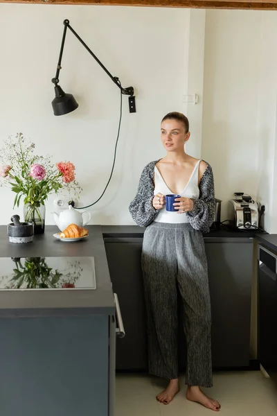 Mujer Positiva Sosteniendo Taza Mirando Lejos Cerca Croissant Cocina Moderna —  Fotos de Stock