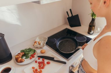 Tavanın üstünde elinde tavayla kiraz domatesleri ve mutfakta yumurtalar olan bir kadın. 