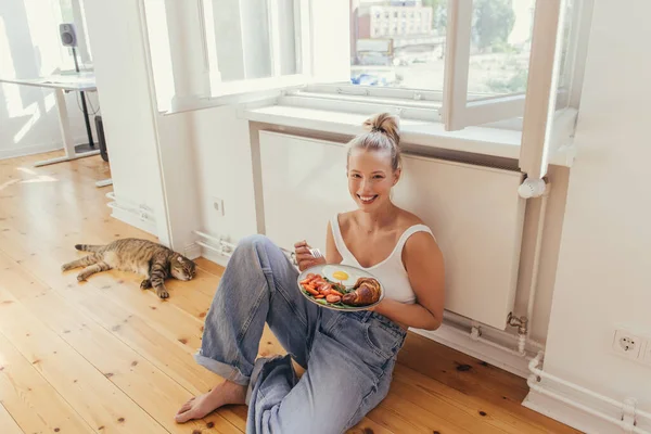 Mujer Joven Positiva Sosteniendo Plato Con Delicioso Desayuno Cerca Gato — Foto de Stock