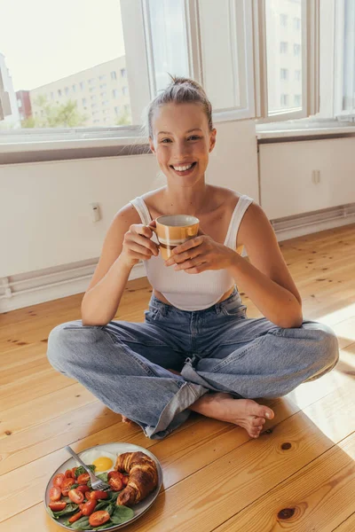 Kot Pantolonlu Elinde Bardakla Gülümseyen Sarışın Kadın Lezzetli Bir Kahvaltıda — Stok fotoğraf