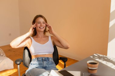Gülümseyen kadın akıllı telefonun yanında yüzüne dokunuyor ve evde kahve içiyor. 