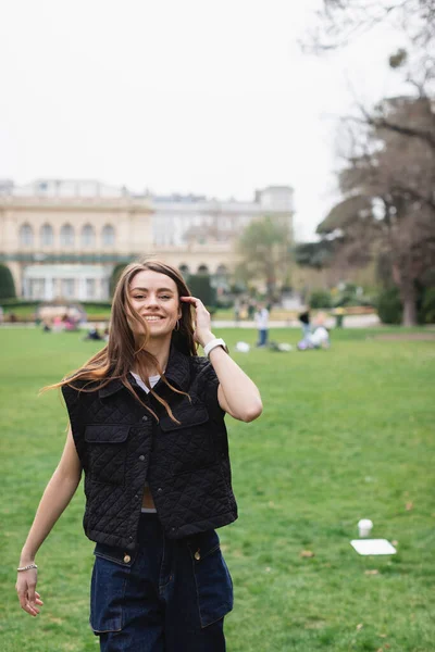 Молода весела жінка в куртці без рукавів в зеленому парку — стокове фото