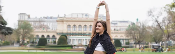 Joven mujer alegre en chaqueta sin mangas que se extiende en el parque verde, pancarta - foto de stock