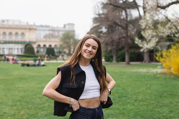 Giovane e sorridente donna in giacca senza maniche nel parco verde — Foto stock