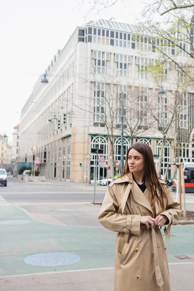 Young woman adjusting belt on stylish trench coat on street of european city — Stock Photo