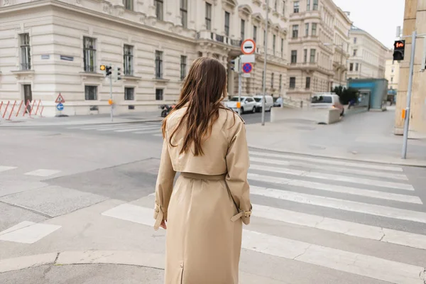 Back view of woman in trench coat walking on street of european city — Stock Photo