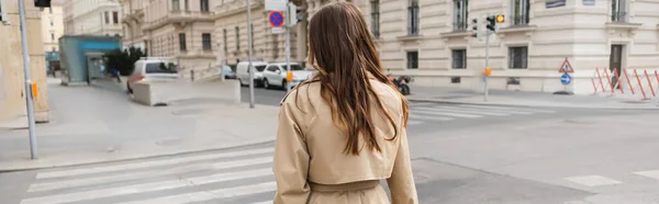 Вид ззаду жінки в траншеї пальто, що йде по вулиці європейського міста, банер — стокове фото