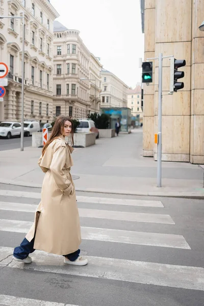 Frau im Trenchcoat passiert Fußgängerüberweg in europäischer Stadt — Stockfoto