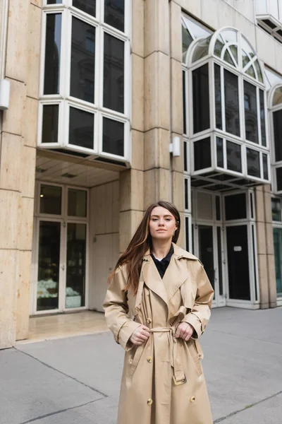 Young woman in stylish trench coat standing near building in vienna — Stock Photo