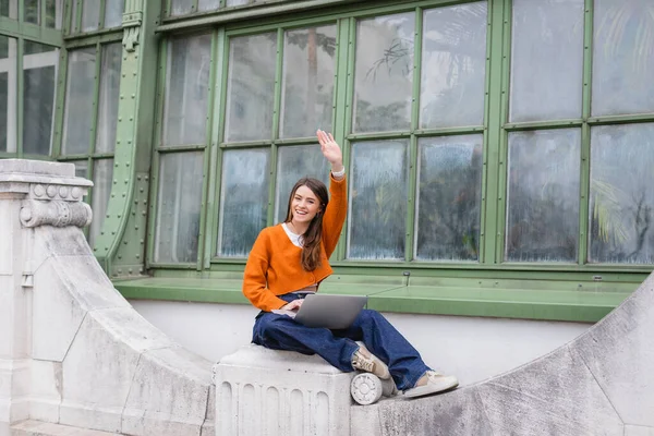 Счастливая молодая женщина машет рукой, пользуясь ноутбуком на крыше здания в Вене — стоковое фото