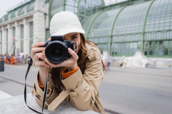 Jovem fotógrafo em casaco de trincheira e boné de beisebol tirar foto na câmera digital — Fotografia de Stock