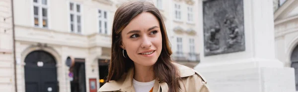 Lächelnde junge Frau im Trenchcoat auf der europäischen Straße, Transparent — Stockfoto