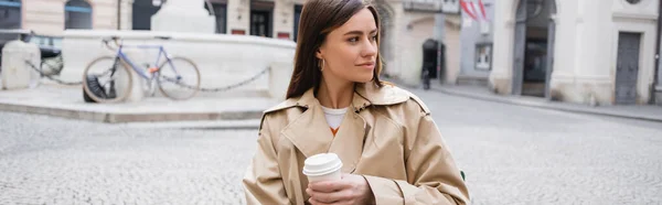 Mujer joven en gabardina de moda sosteniendo café para llevar, pancarta - foto de stock